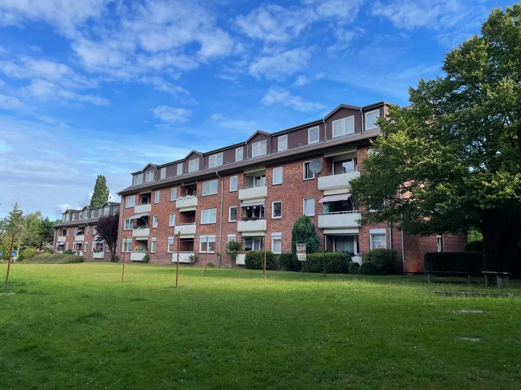 Ansicht eines Mehrfamilienhauses aus Backstein mit Balkonen vor blauem Himmel und mit einer grünen Wiese im Vordergrund